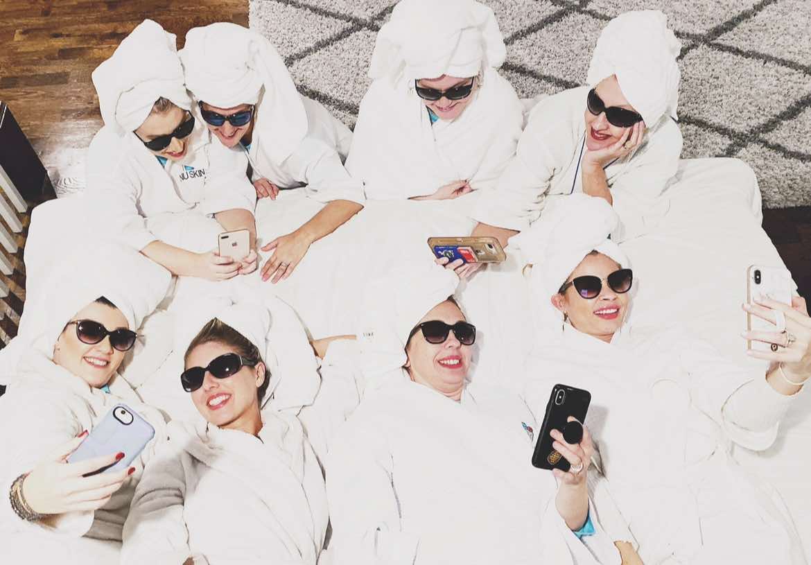 Group of women in bath robes and towels on their heads taking a selfie.