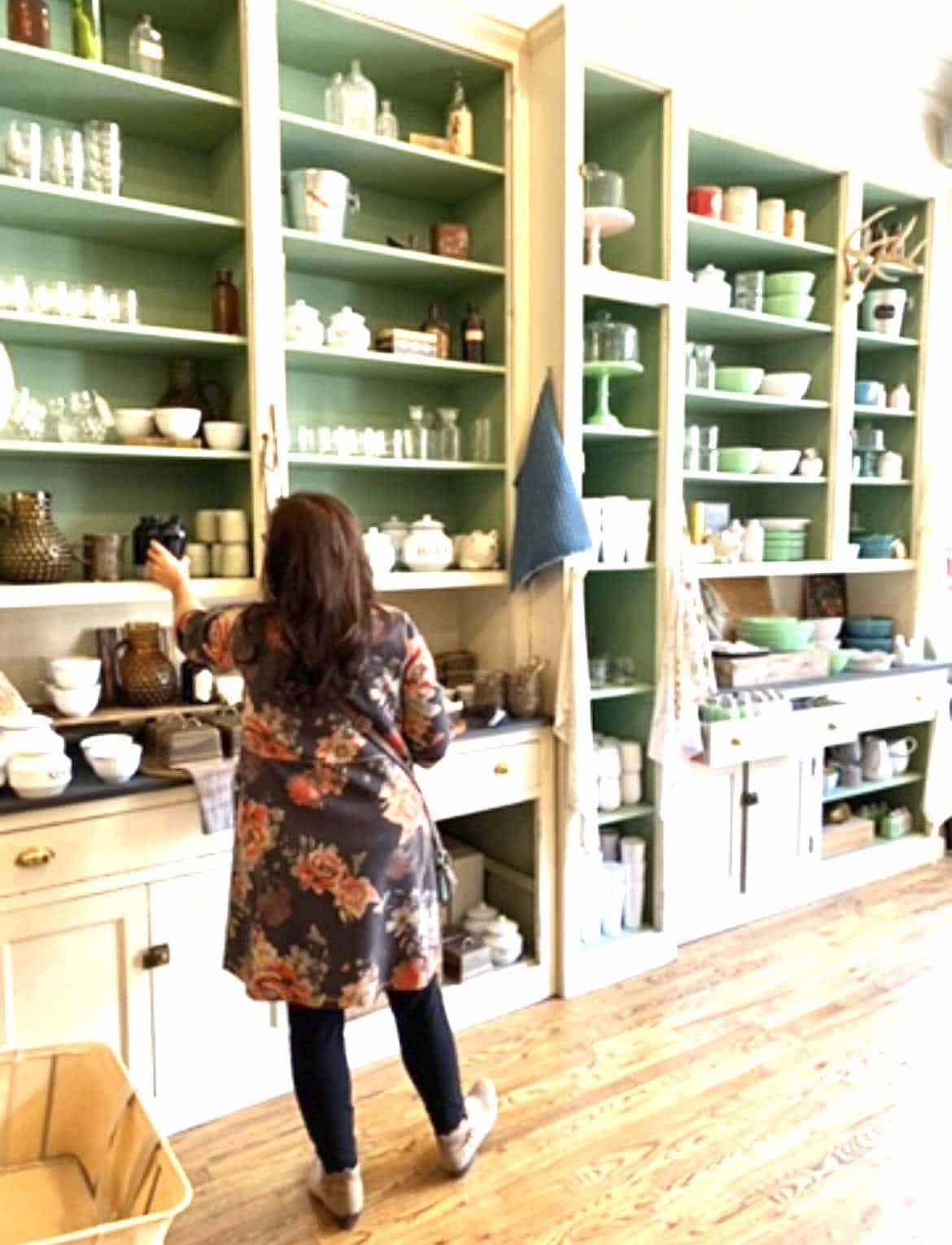 Woman shopping in a store that has white shelves with green walls.