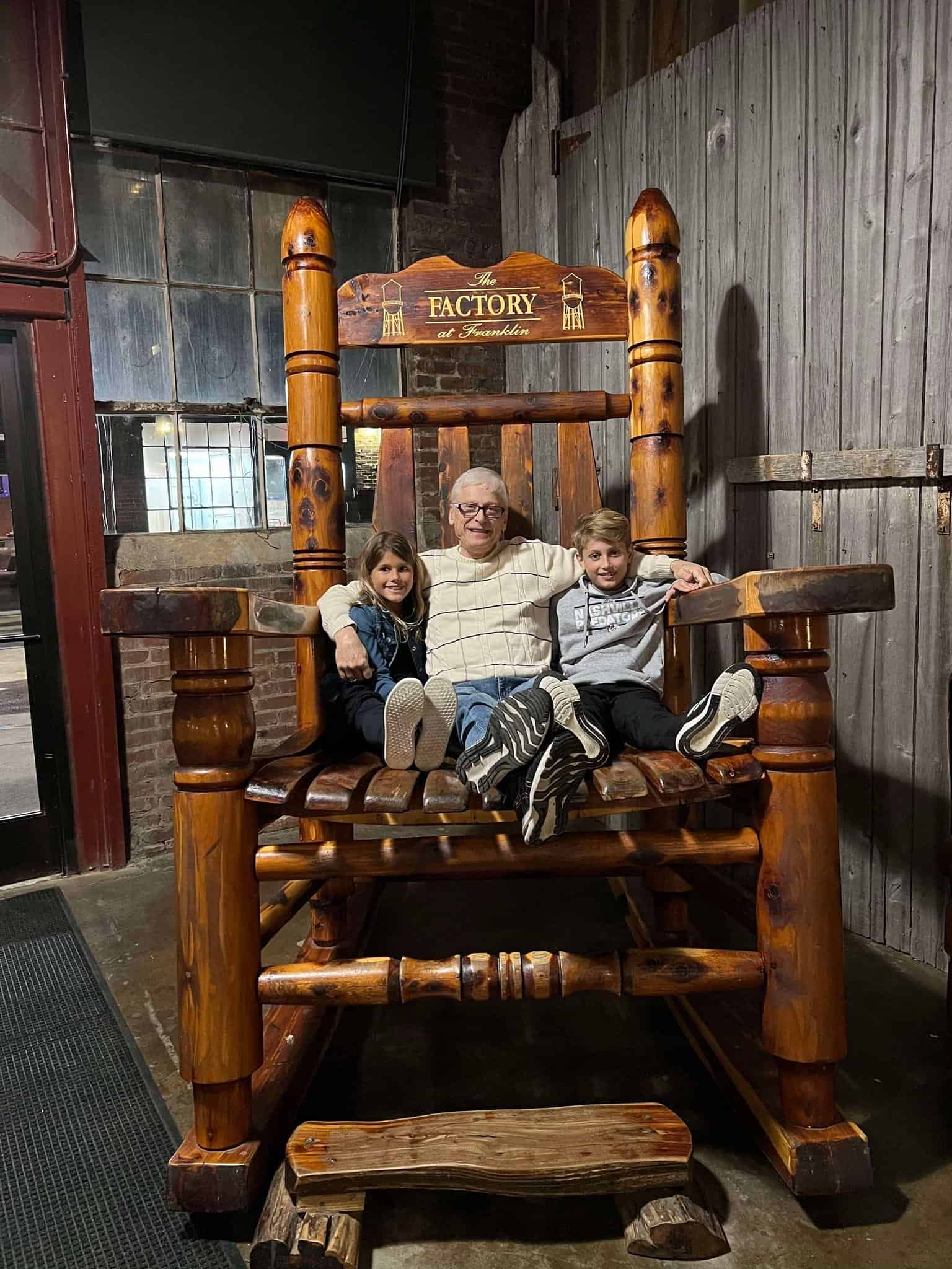 A man with his two grandchildren in a very large rocking chair that holds all 3 of them.