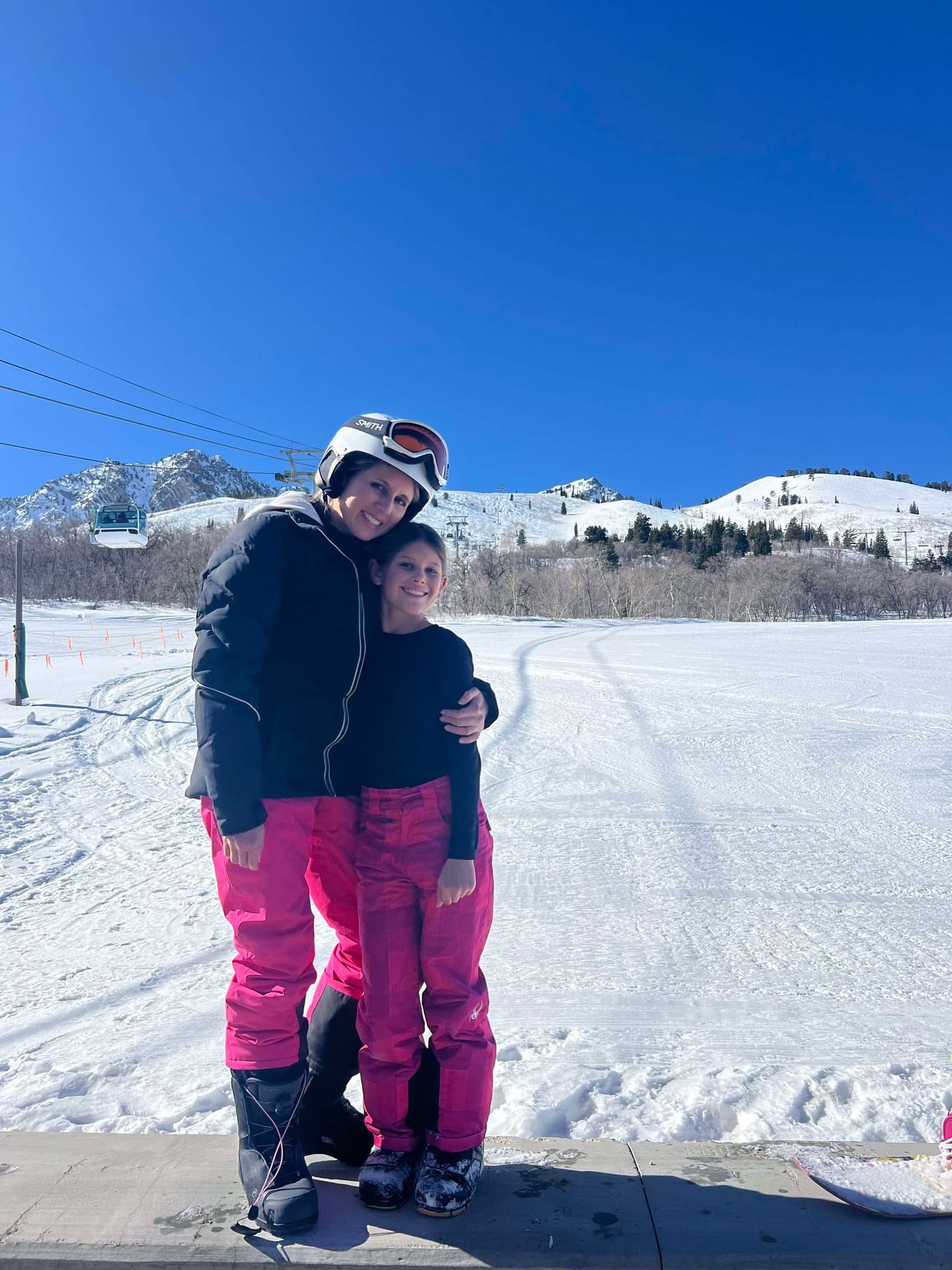 A mom and daughter match with their pink snowboard pants and black tops. They are hugging at the Strawberry Patio while taking a rest.