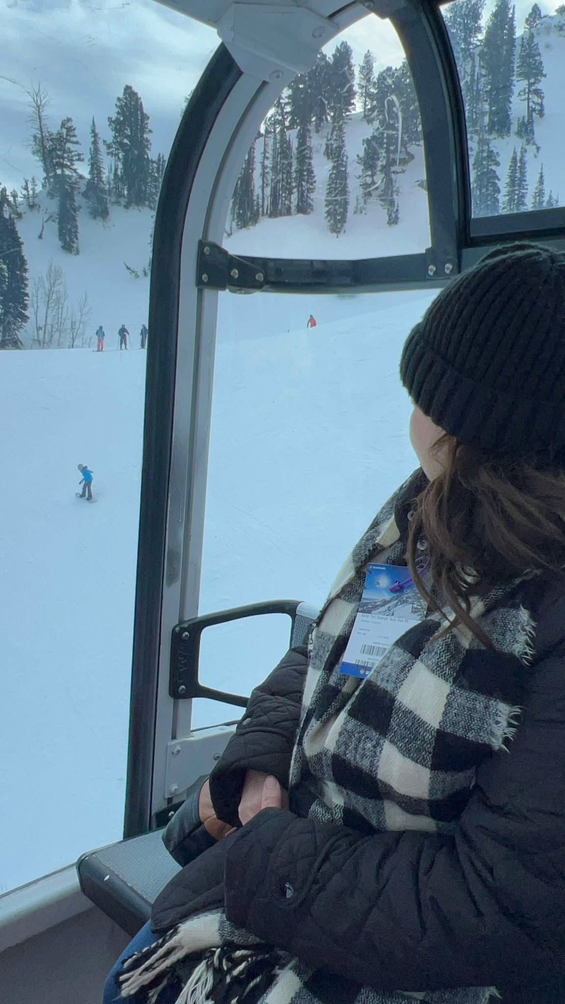 A grandma rides the gondola and watches her grandson snowboard below her.