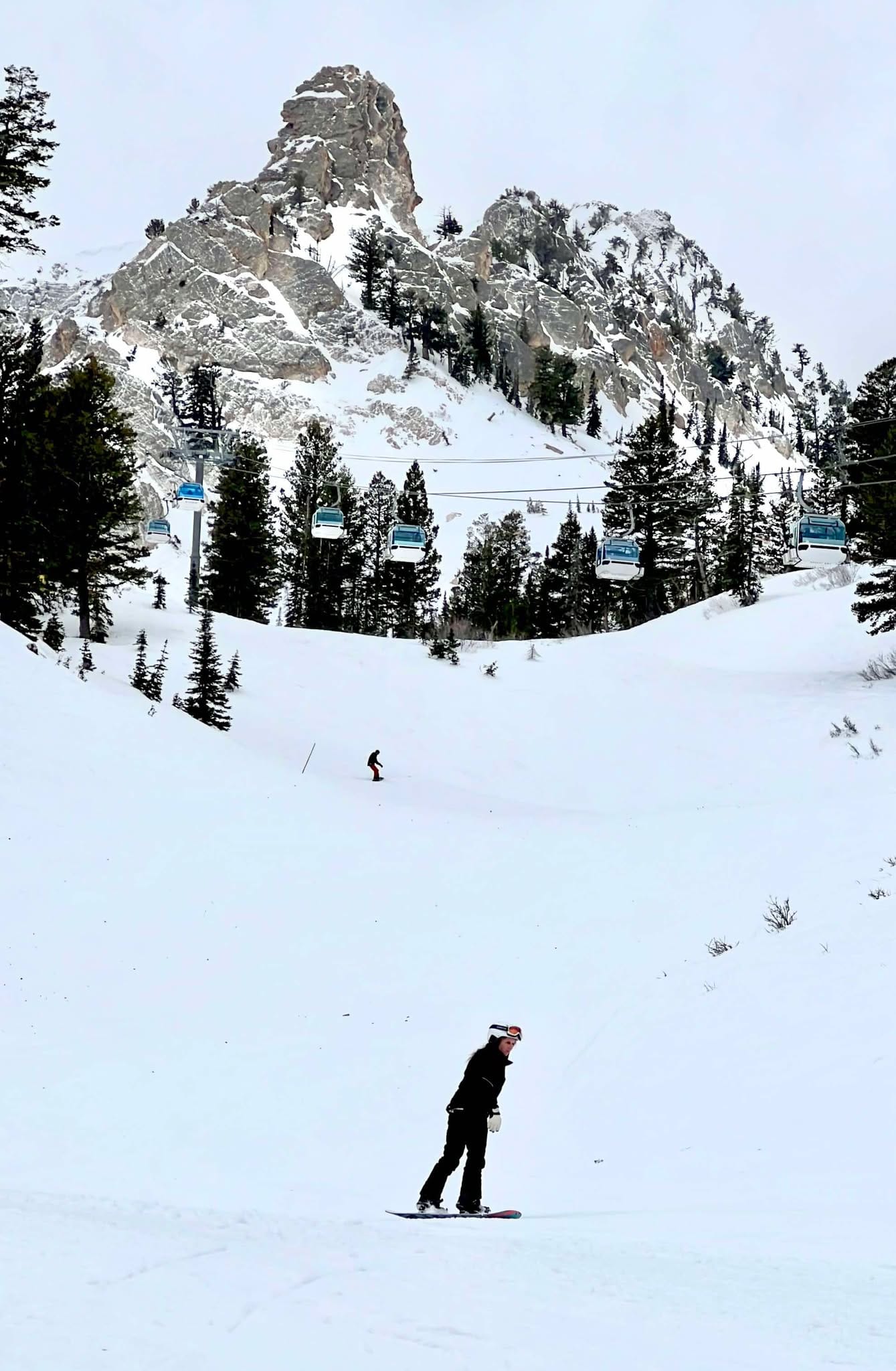 A mom snowboarding with a pointy rocky face behind her on a family snowboarding trip to Snowbasin Ski Resort.