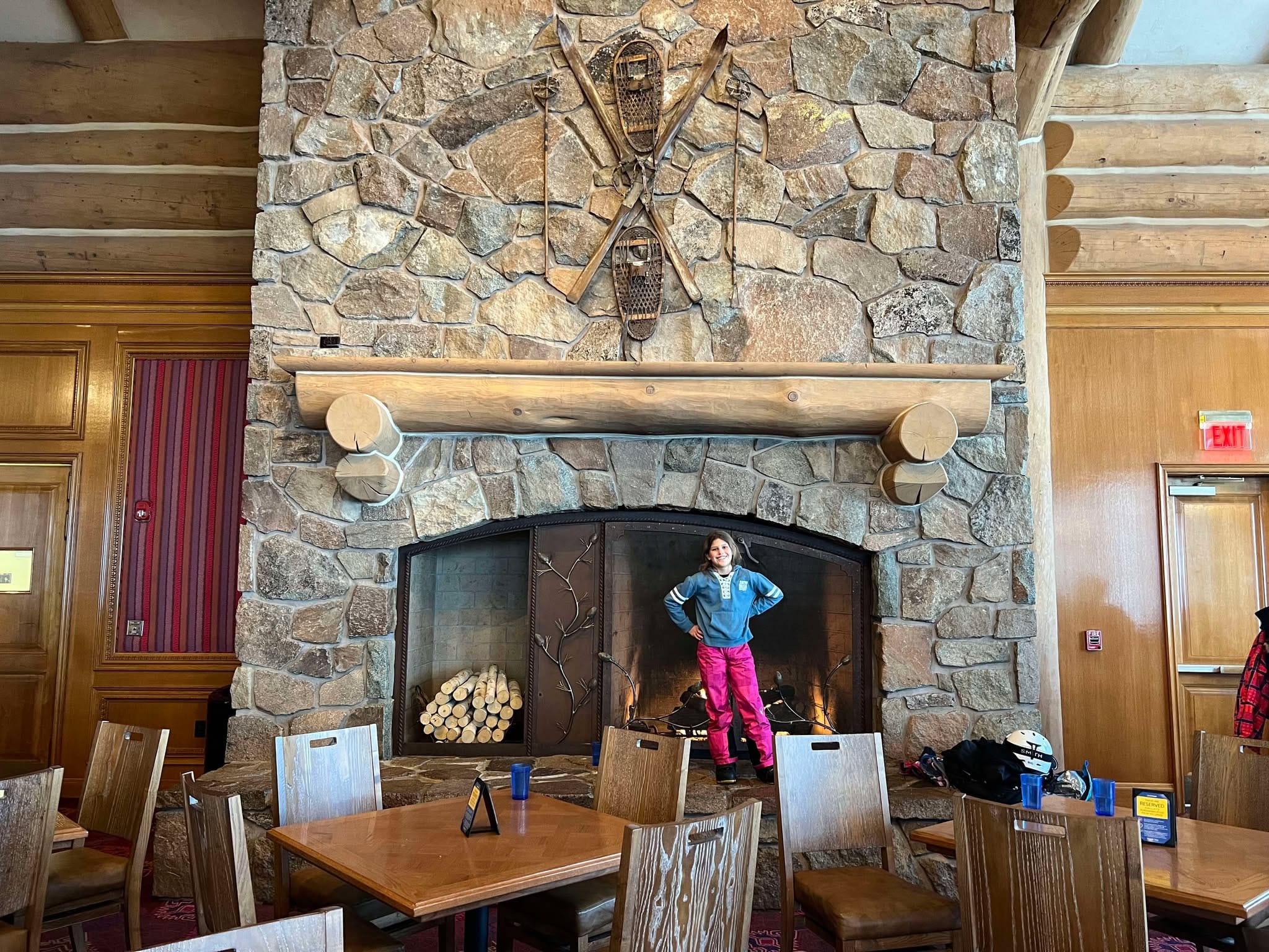 Little girl standing in front of the massive, stone fireplace in Earl's Lodge at Snowbasin.