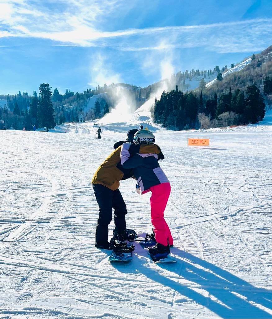 A guy and a girl hugging after he taught her how to snowboard during their family trip to Snowbasin.