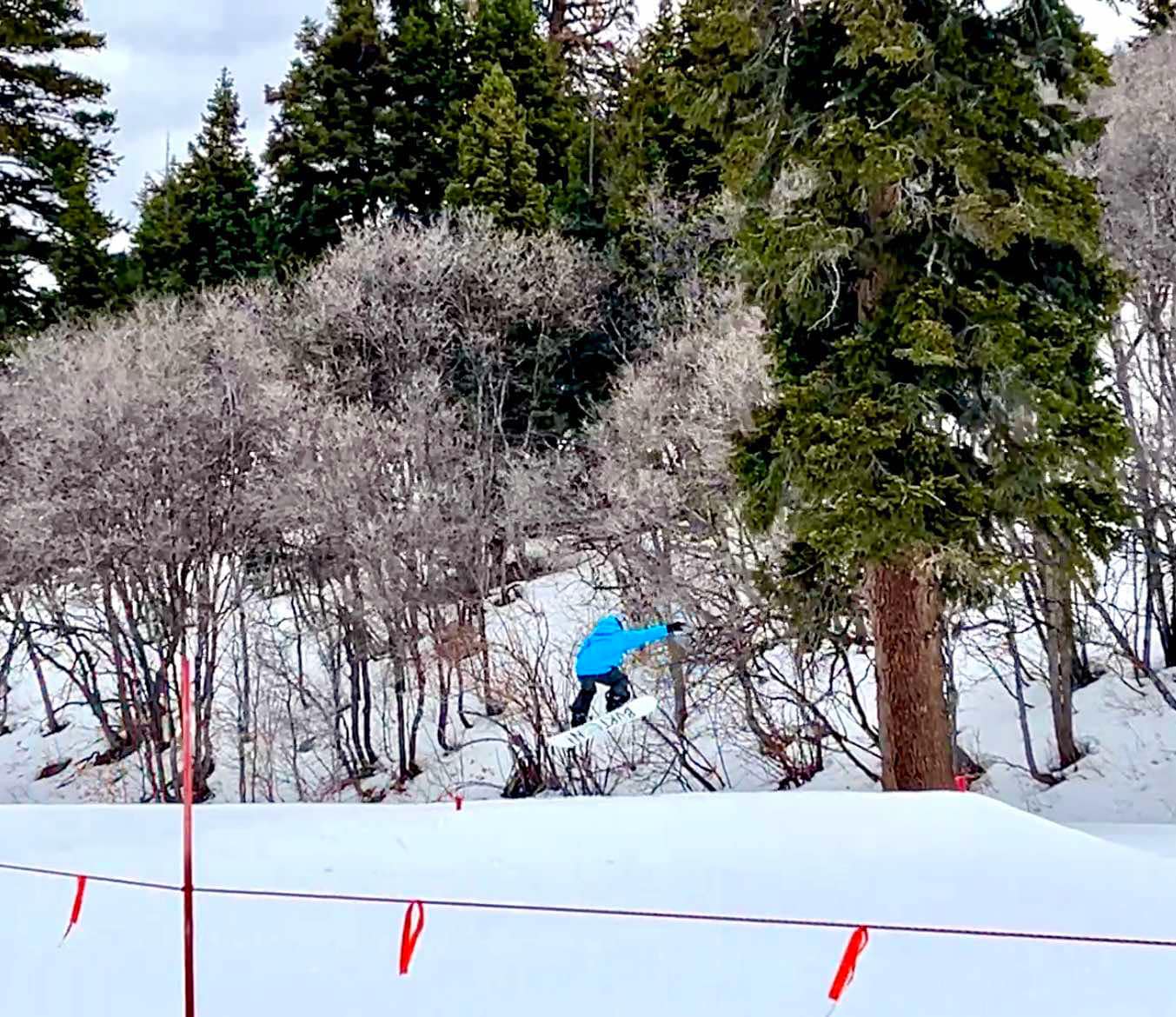 Boy in blue coat jumping a hill on a terrain park during a family snowboarding vacation at Snowbasin Ski Resort.