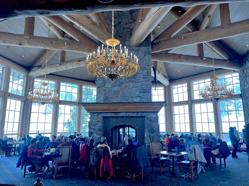A view of the dining room at John Paul Lodge at Snowbasin with a massive fireplace in the middle.