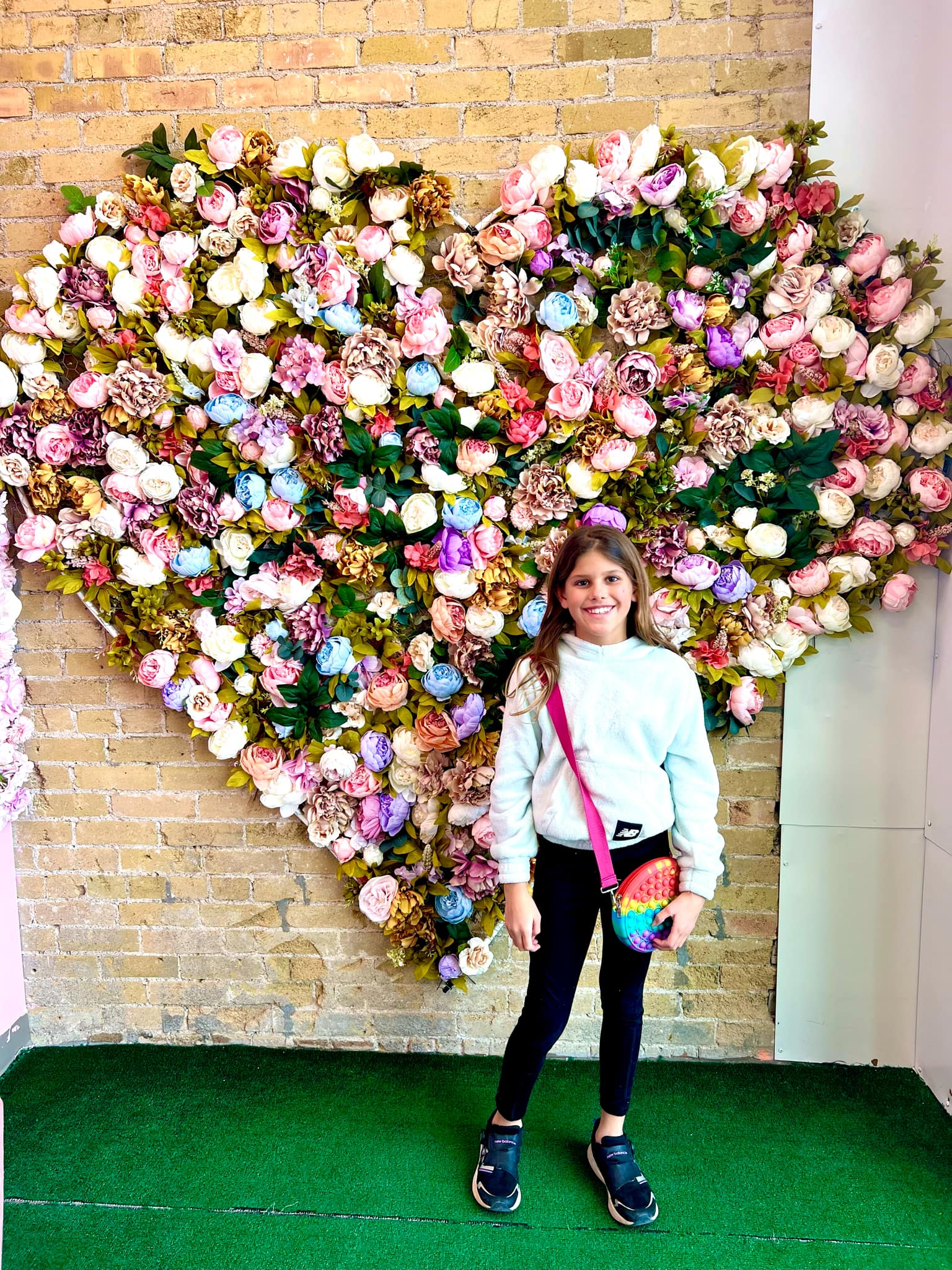 A girl standing in front of a heart made out of flowers.