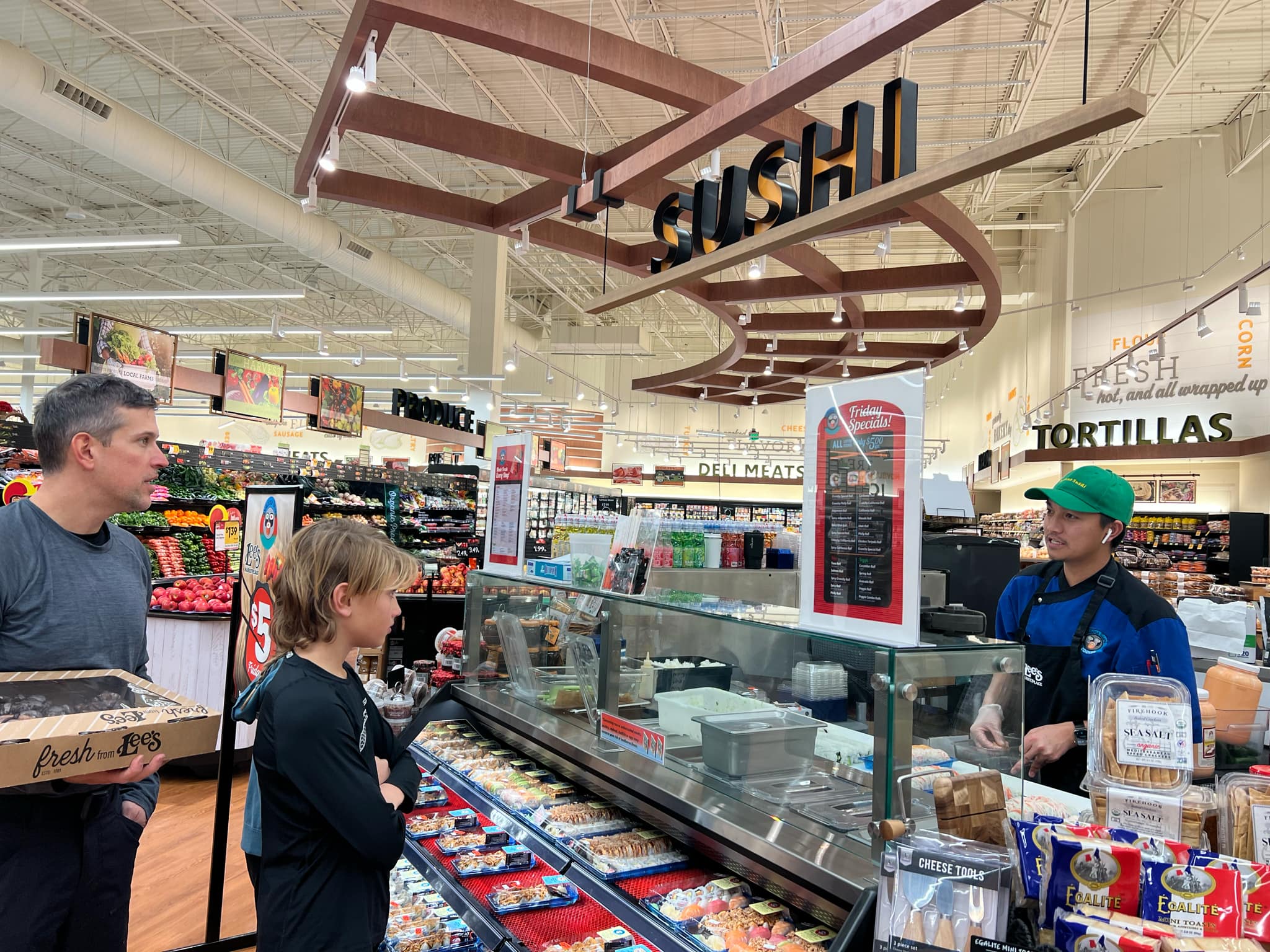 A family gets sushi at the local grocery store. There is a man making the sushi fresh.