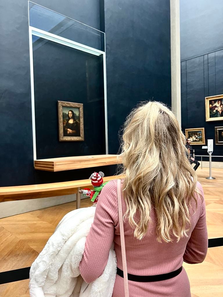 Girl in pink dress holding a little stuffed mouse looking at the Mona Lisa for this free things to do in Paris picture.
