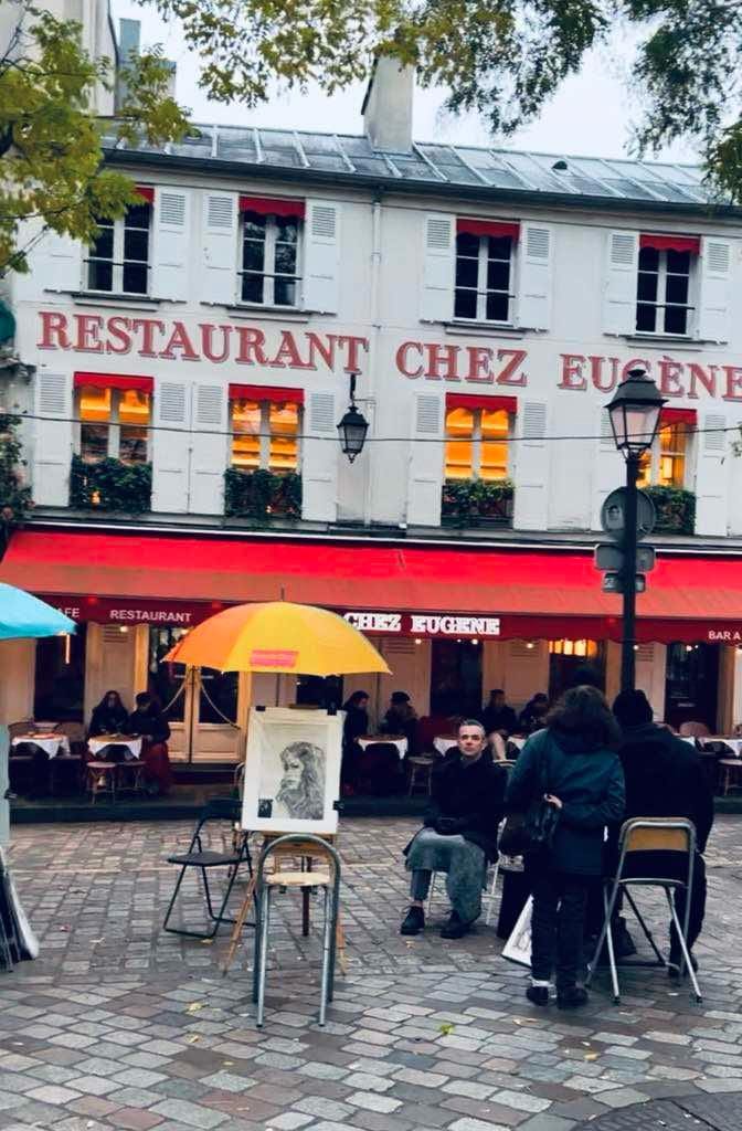 An artist working on a portrait in Montmartre with a cafe behind it.