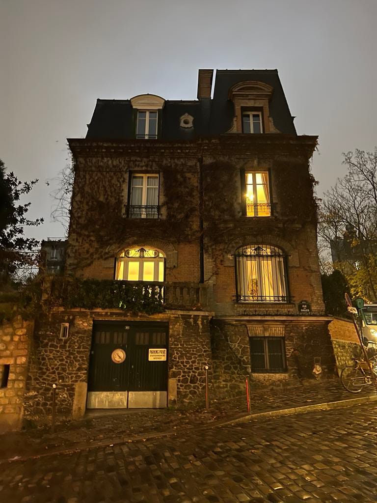 An eerie looking building in Montmartre at night. It looks eerie because of the vines covering it, but it also looks romantic with the lights on the inside that are shining through the windows.