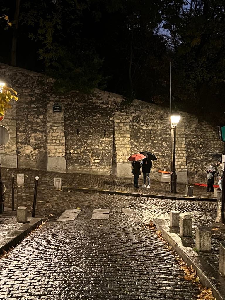 Two people holding umbrellas on a cobblestone street in Montmartre.