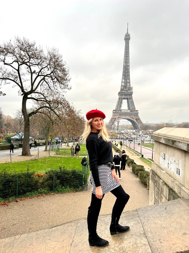 Girl in black and white skirt, black sweater and red hat posing in front of the Eiffel Tower in Paris.