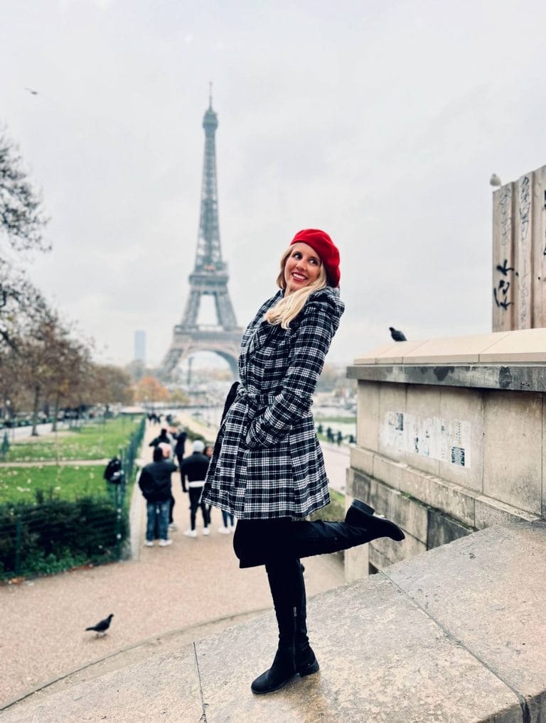 Girl in black and white coat with red hat in front of the Eiffel Tower in Paris.