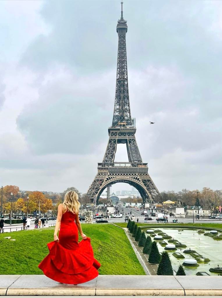 Girl in long, fancy red dress twirling in front of the Eiffel Tower in Paris.