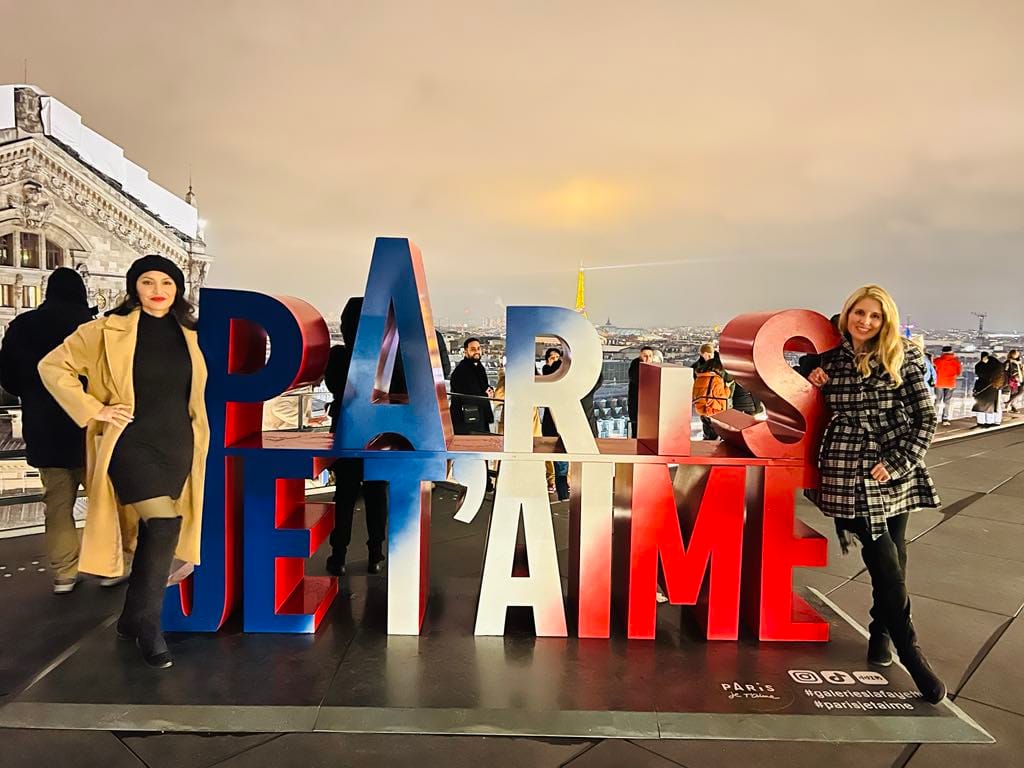 This picture of free things to do in Paris is of two girls taking a photo with the 'Paris Je T'aime" sign on the rooftop of the Galeries Lafayette.