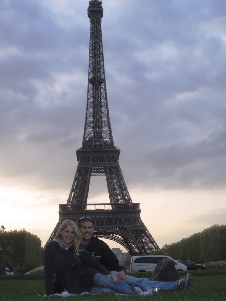 Guy and girl sitting on a towel for a picnic at the Eiffel Tower.
