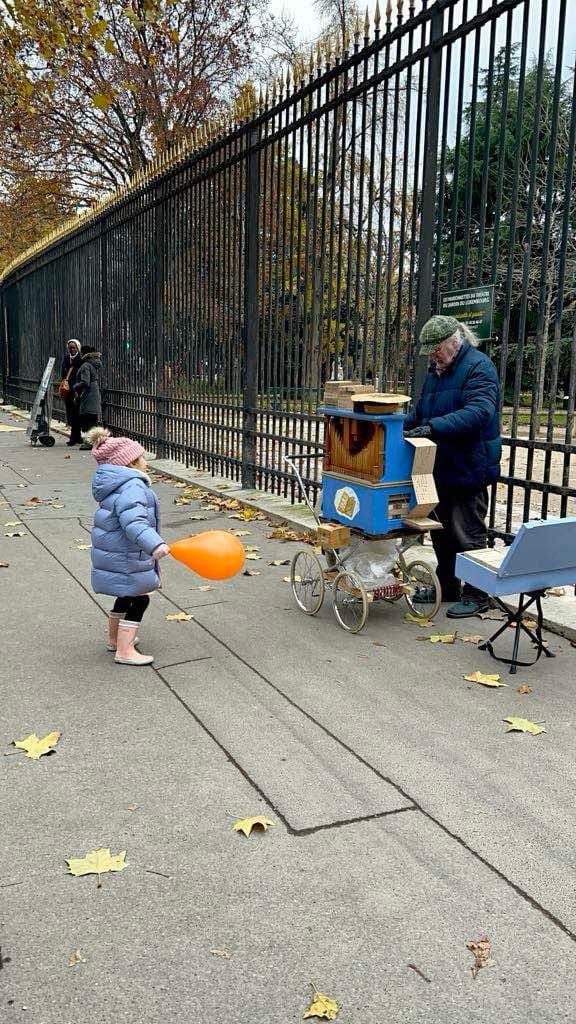 Little girl holding an orange balloon dancing while a French man plays music for her on a music box.