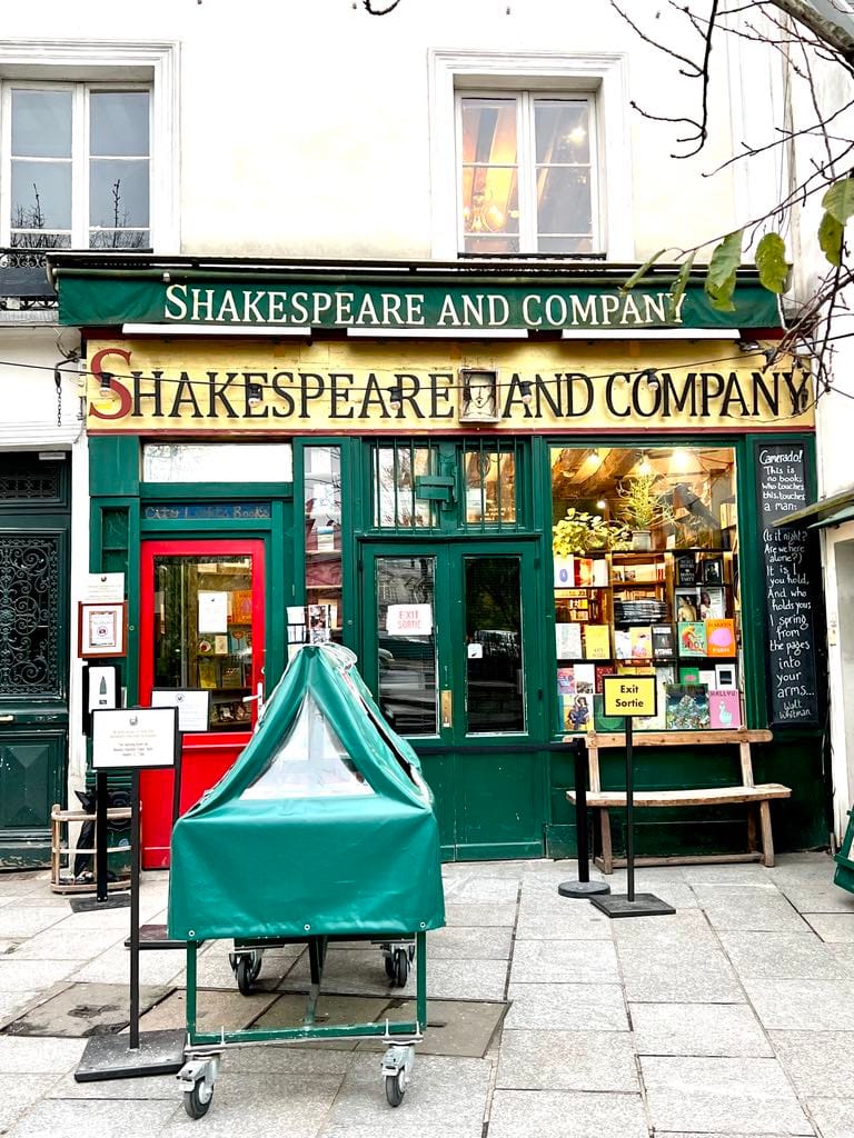 Photo of the outside of Shakespeare & Co bookstore. Bookstore is green with a red door and is free entry.