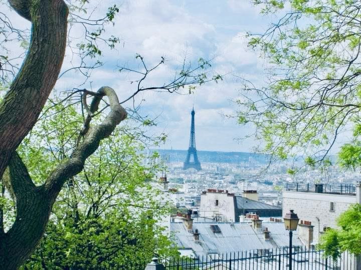Picture of the Eiffel Tower from the Montmartre hill. The Eiffel is off in the distance and out of focus, while the green trees are framing it and are in focus.