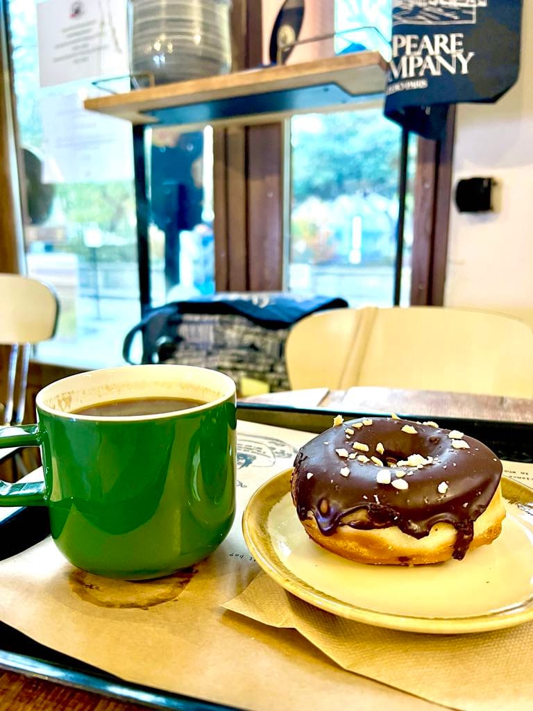 Picture of a green coffee mug and chocolate donut at the Shakespeare & Co coffee shop.