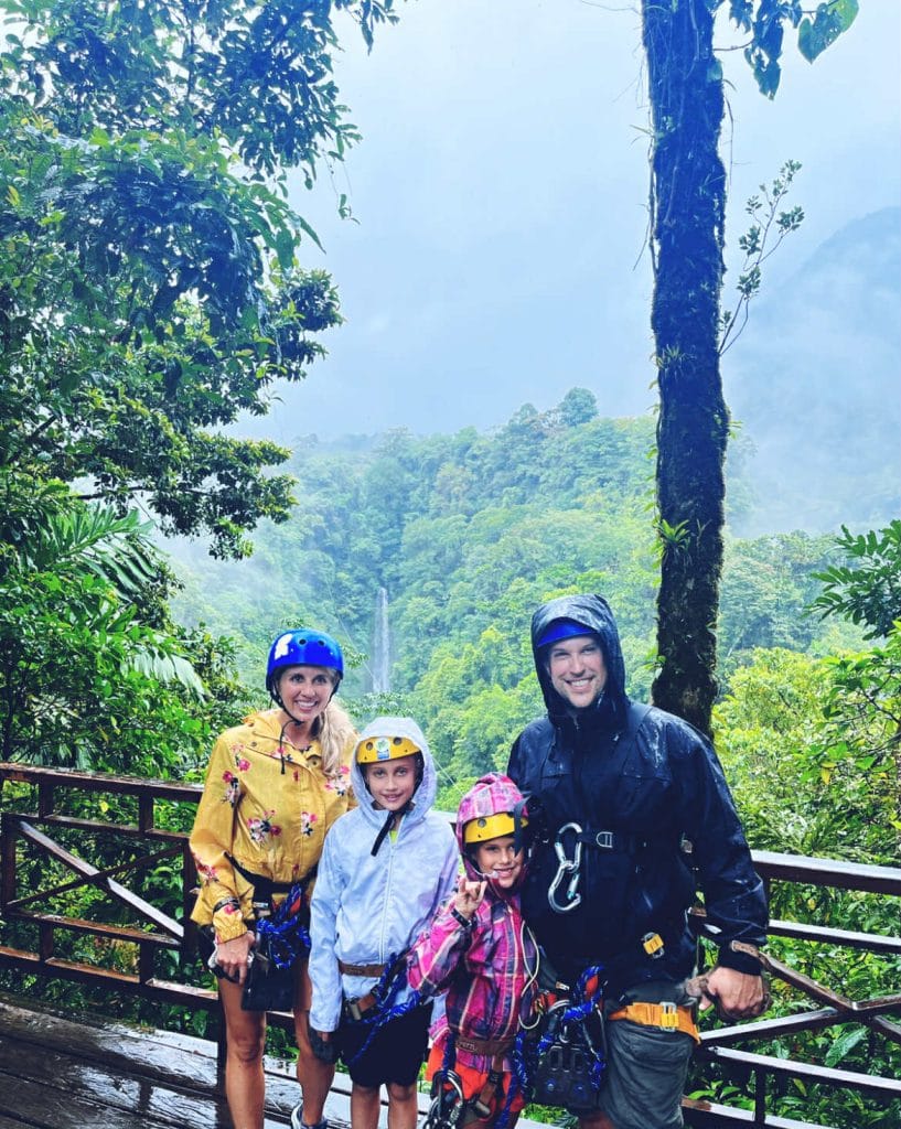 Family with rain coats on about to zip line with the lush rain forest behind them.