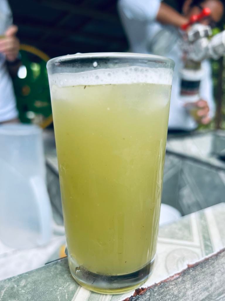 A full glass of sugar cane juice. It is a muted yellow color with some foam at the top.