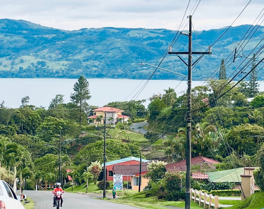 Two kids riding a moped in Costa Rica with the lake and houses behind them.