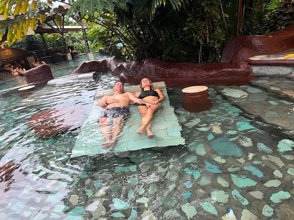 A mom and dad laying on a hot stone in the hot springs at Baldi Resort while on a Costa Rica with Kids trip.
