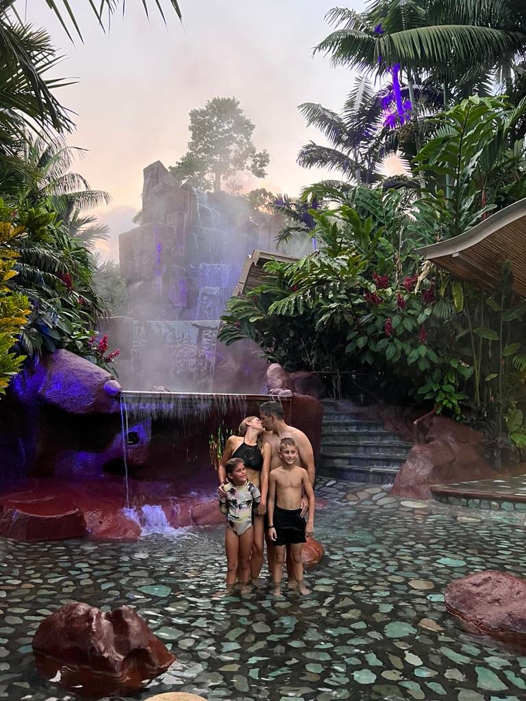 A mom and dad kissing while the two kids are in front of them and the back drop is a big waterfall at the Baldi Resort in Costa Rica.