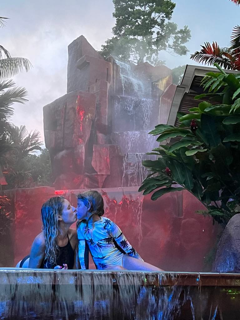 A mom and daughter kissing while laying in the hot spring with a waterfall behind them at the Baldi Hot Springs in Costa Rica.
