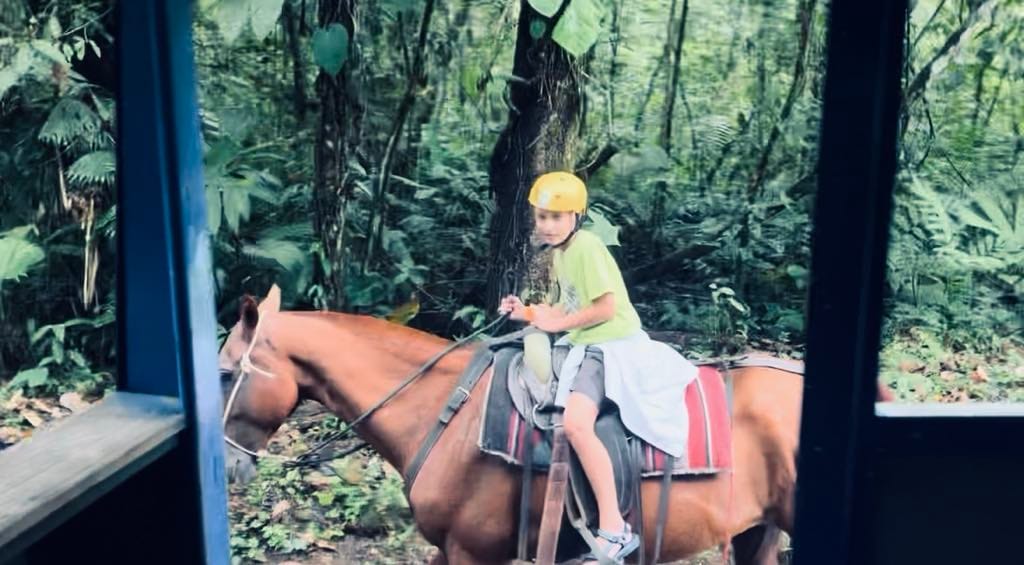 Boy in green shirt riding a horse next to a bus after zip-lining.