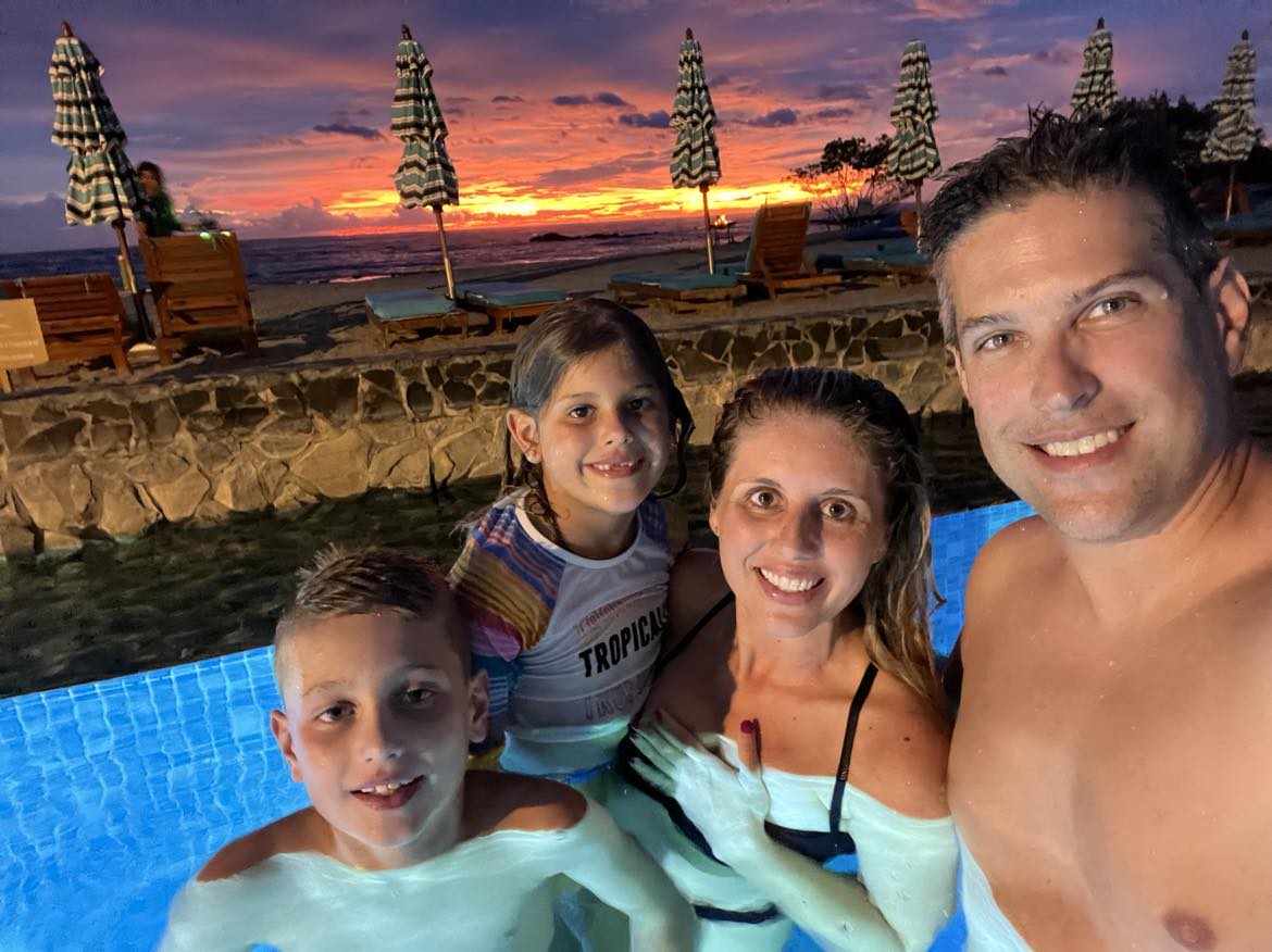 A family in the pool with the orange sunset behind them while on their Costa Rica with kids vacation.