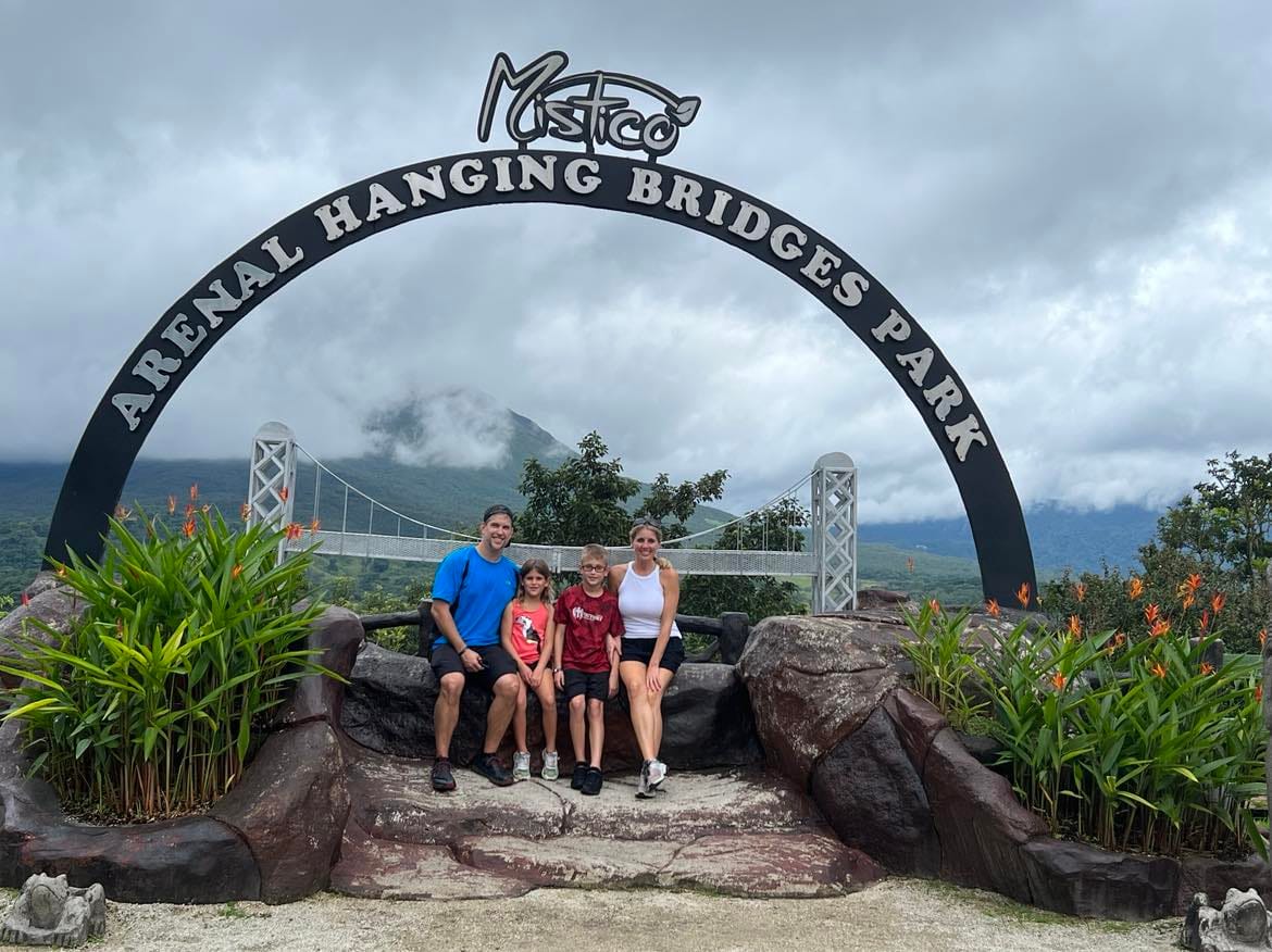 Mom, dad and kids at the Arenal Forest hike with the Arenal sign behind them in a half-circle shape.