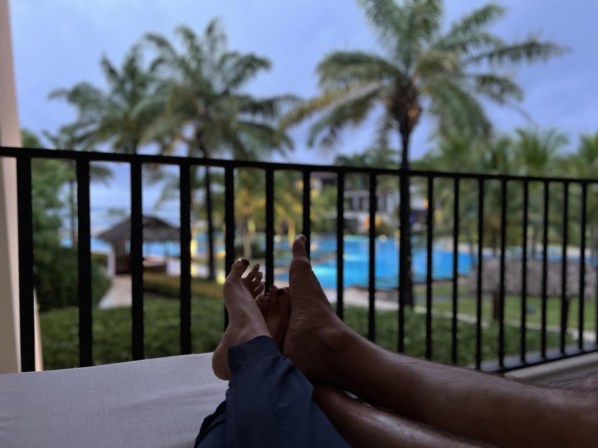 A man and woman's feet snuggled while they are sitting on a balcony watching the sunrise.