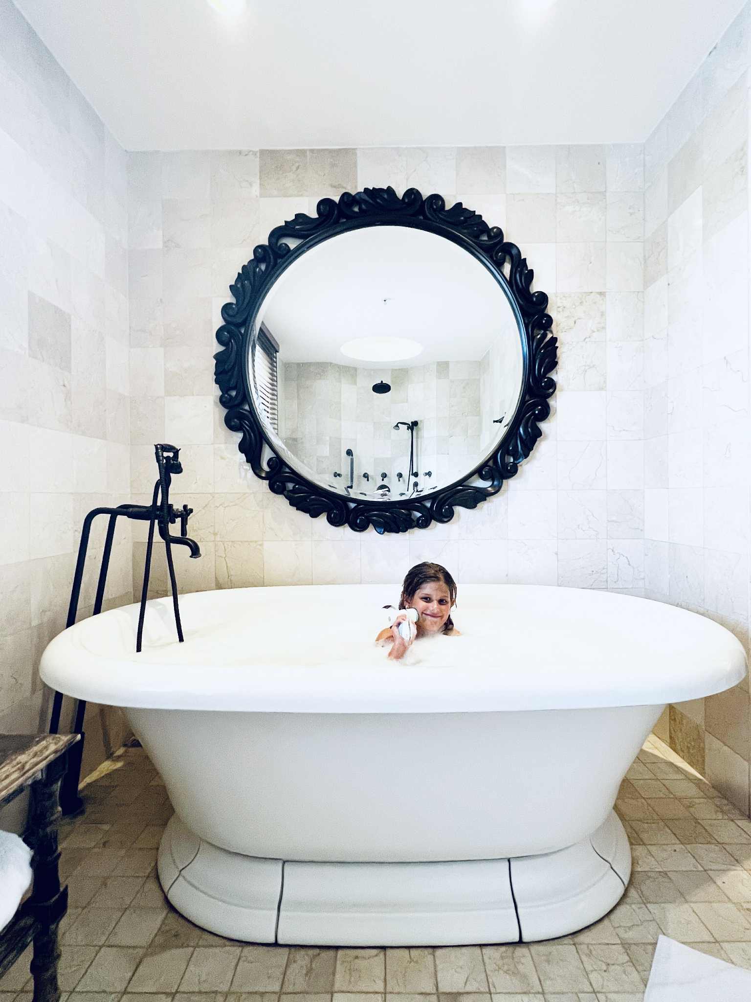 A girl in a bubble bath in a massive, gorgeous bathtub.