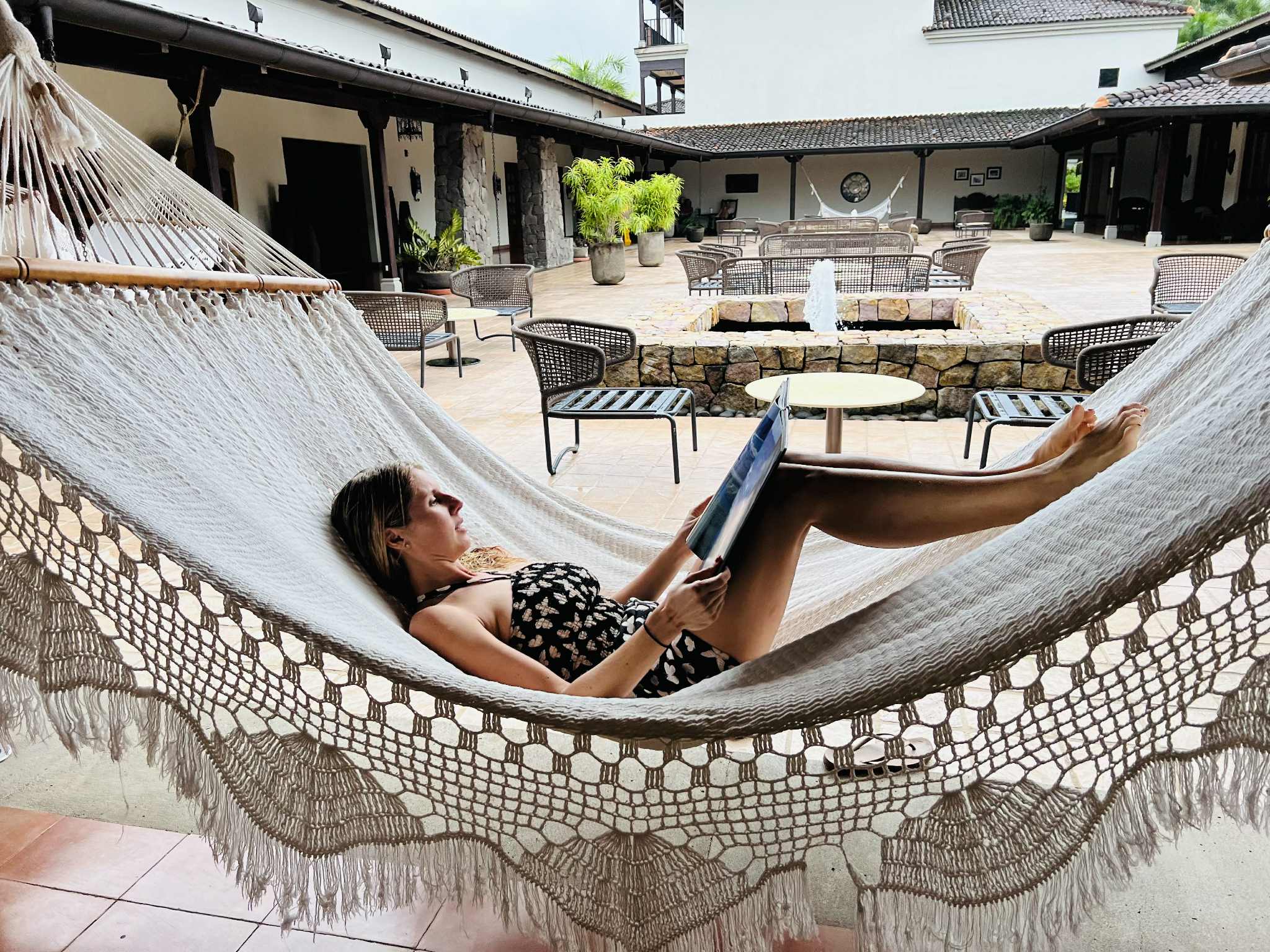 A mom relaxing on her vacation to Costa Rica with kids. She is on a hammock reading a book with a courtyard behind her.