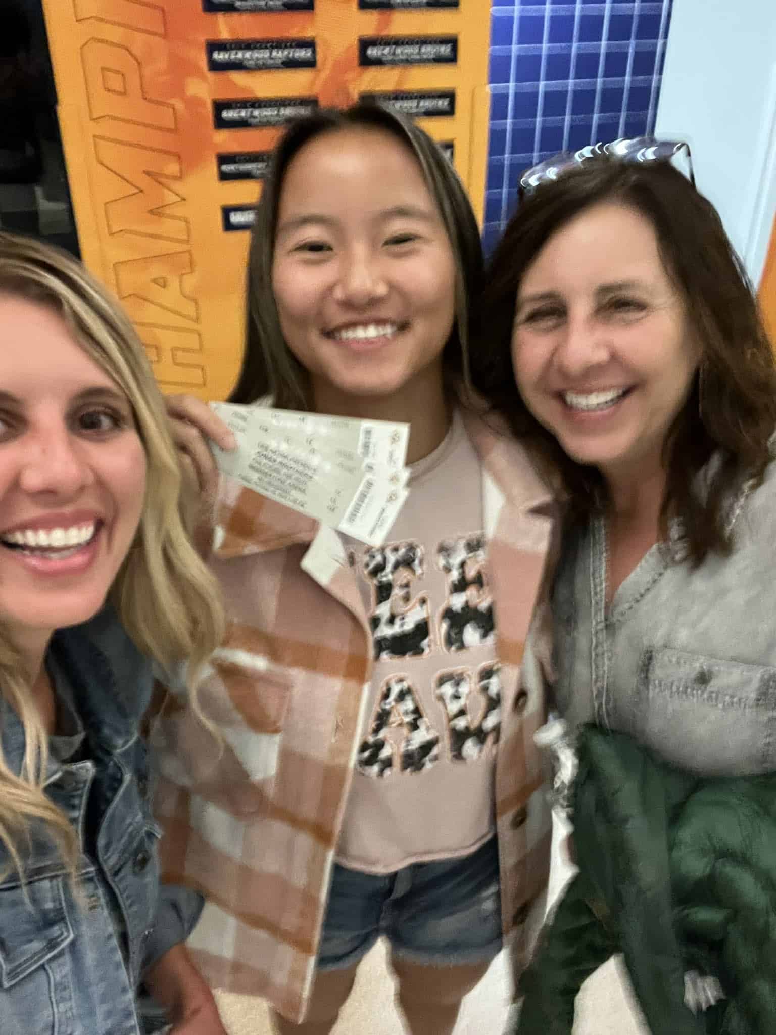 A teenager with her mom and sister in Nashville going to a concert. She is holding up her concert tickets for the picture.