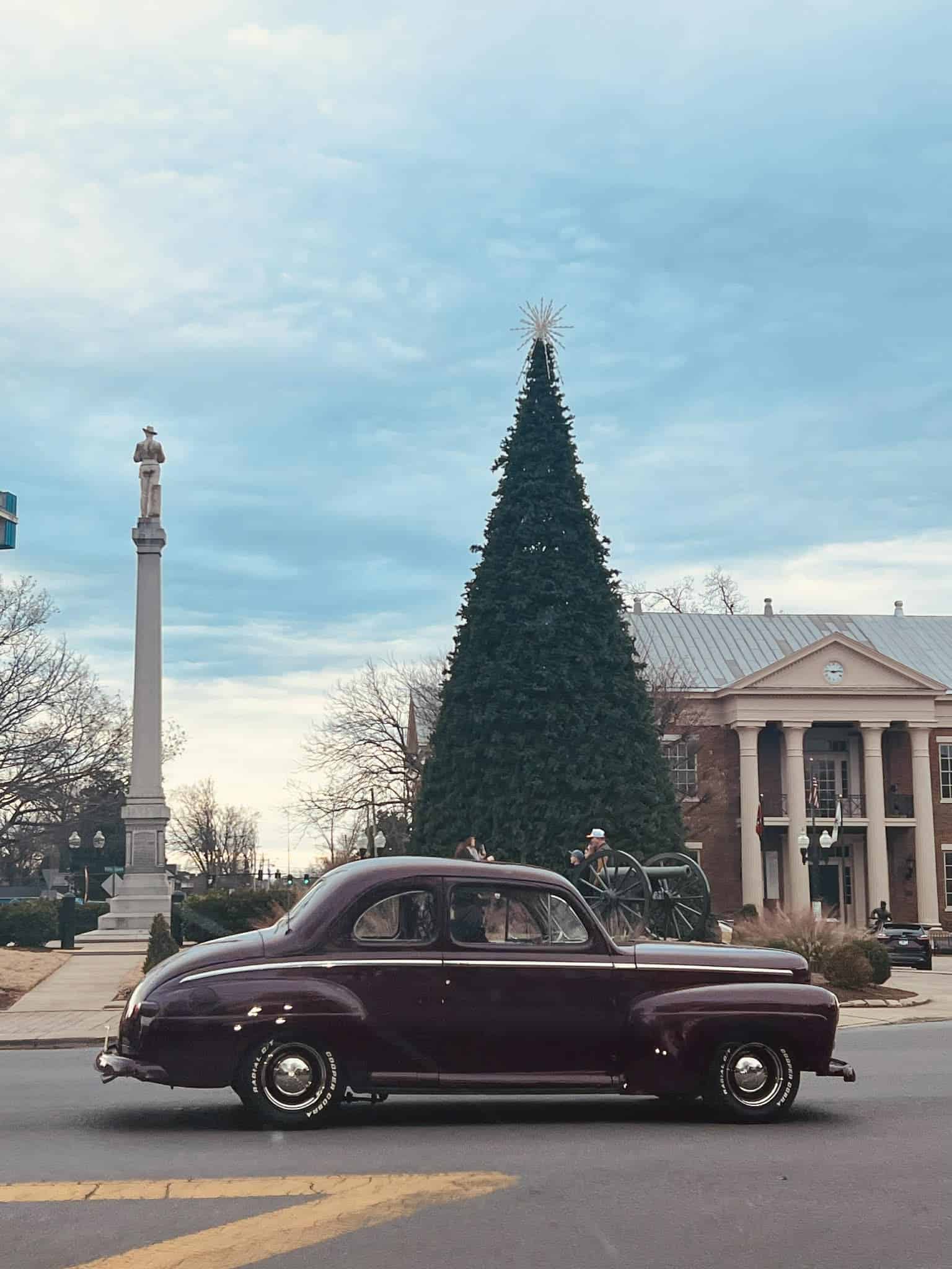 An old car passing through the downtown Franklin square while the town's Christmas tree is up in the square.