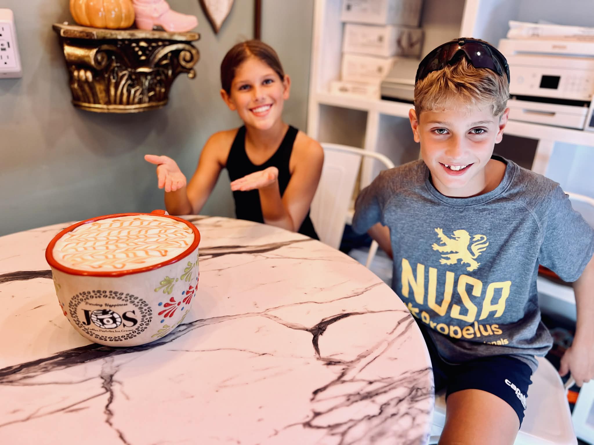 Two kids with a huge coffee in front of them.