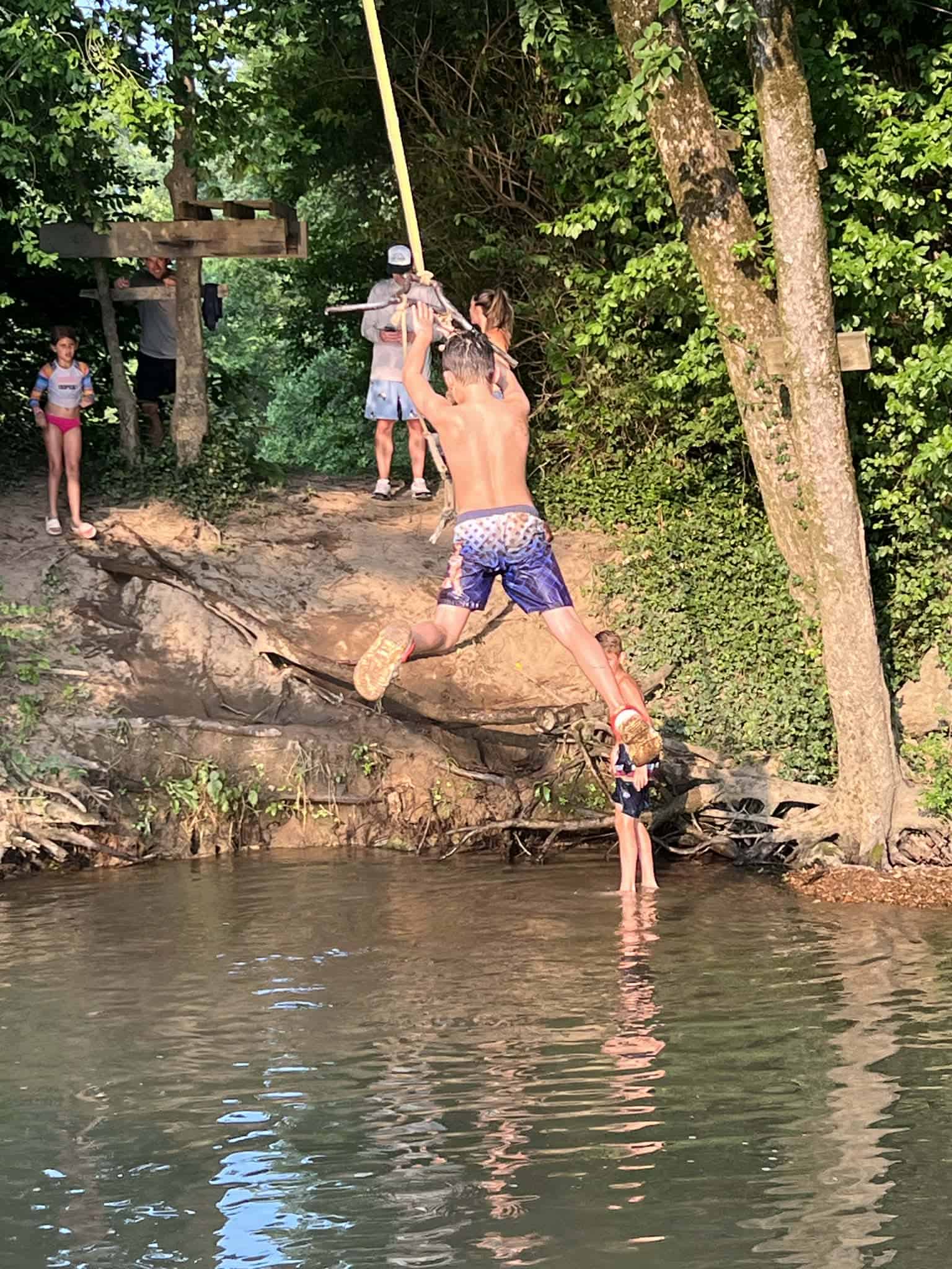 A boy swinging from a rope swing into a creek.