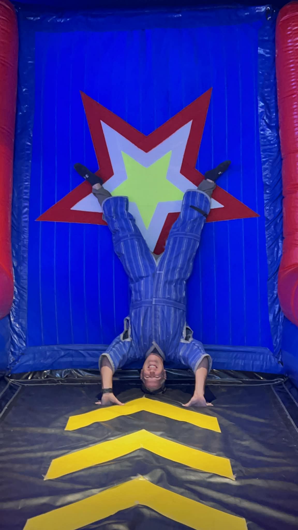 A dad has on a velcro suit and doing a handstand on the velcro wall at Play Playground in Nashville.