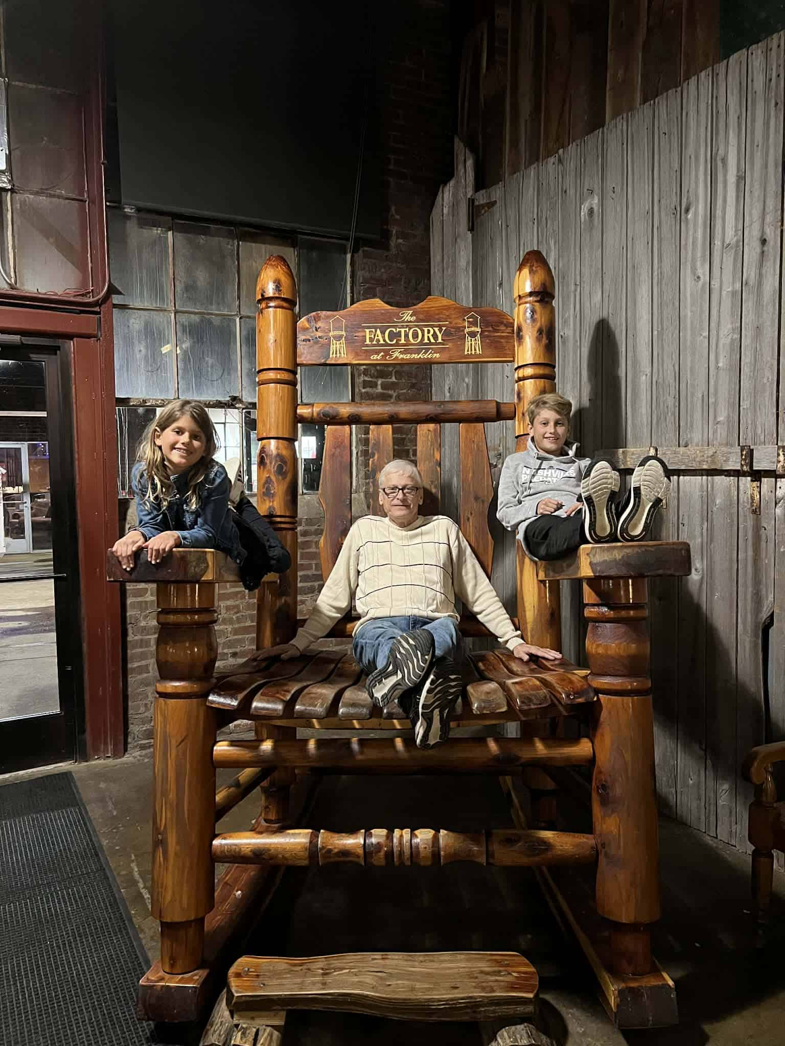 A grandpa and two kids sitting on a large rocking chair.