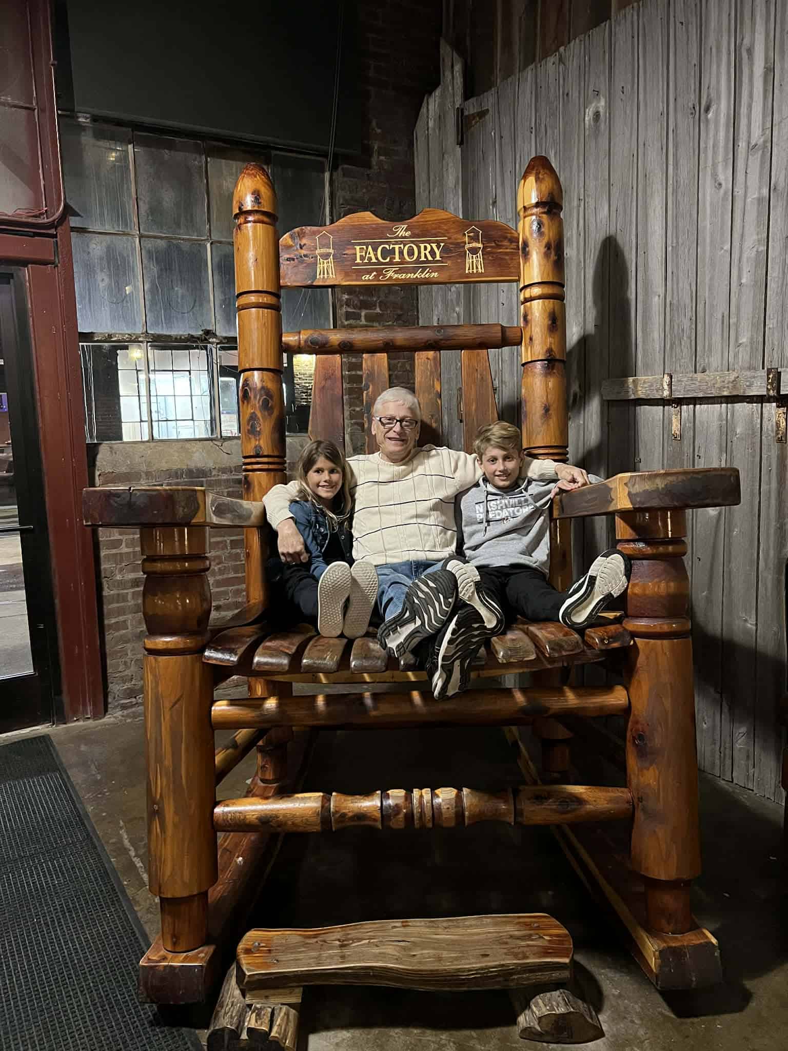 A grandpa and two kids sitting on a very large rocking chair.