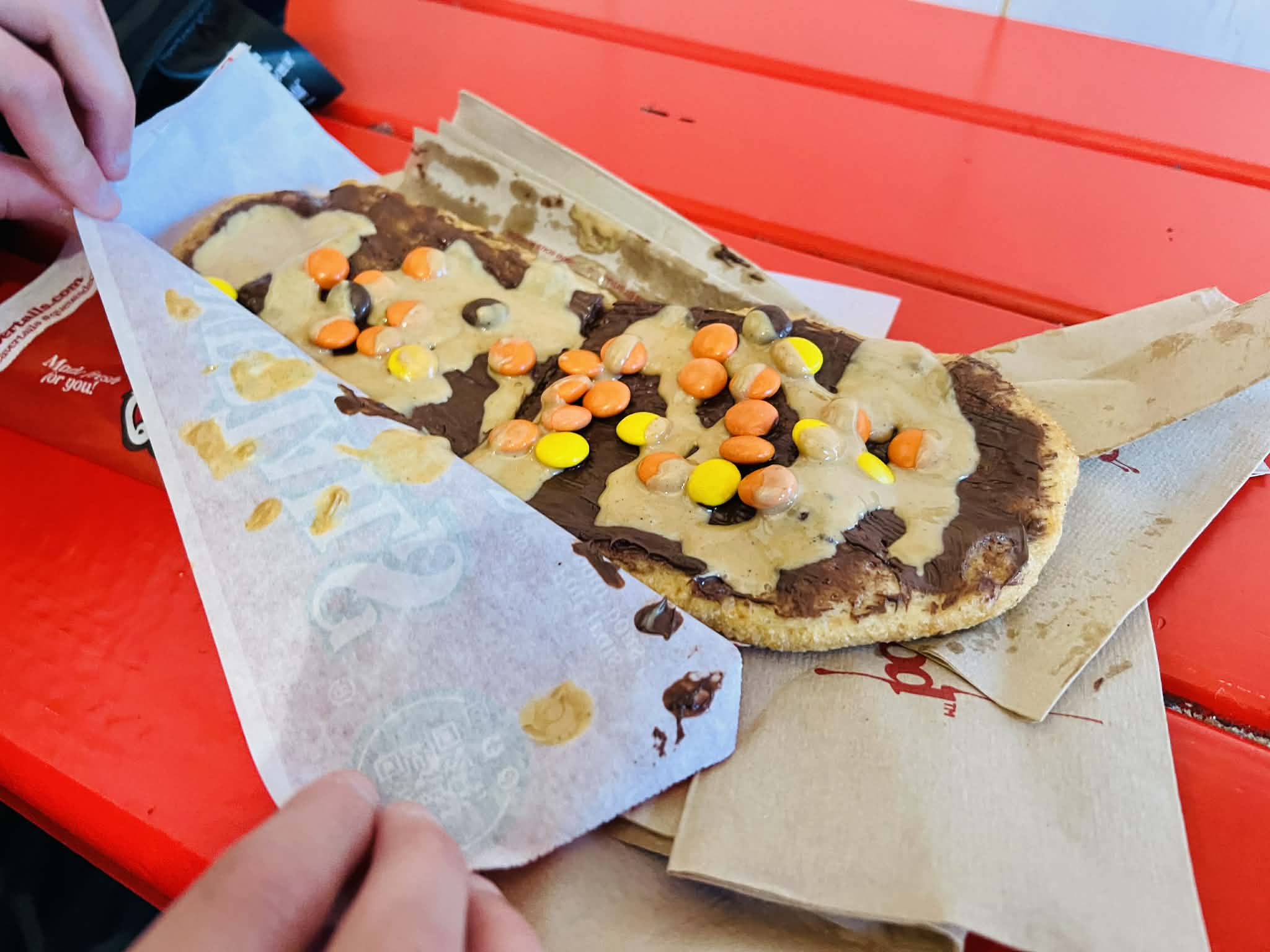 A peanut butter Reece's pieces fried dough treat called a Beaver Tail on a red table.