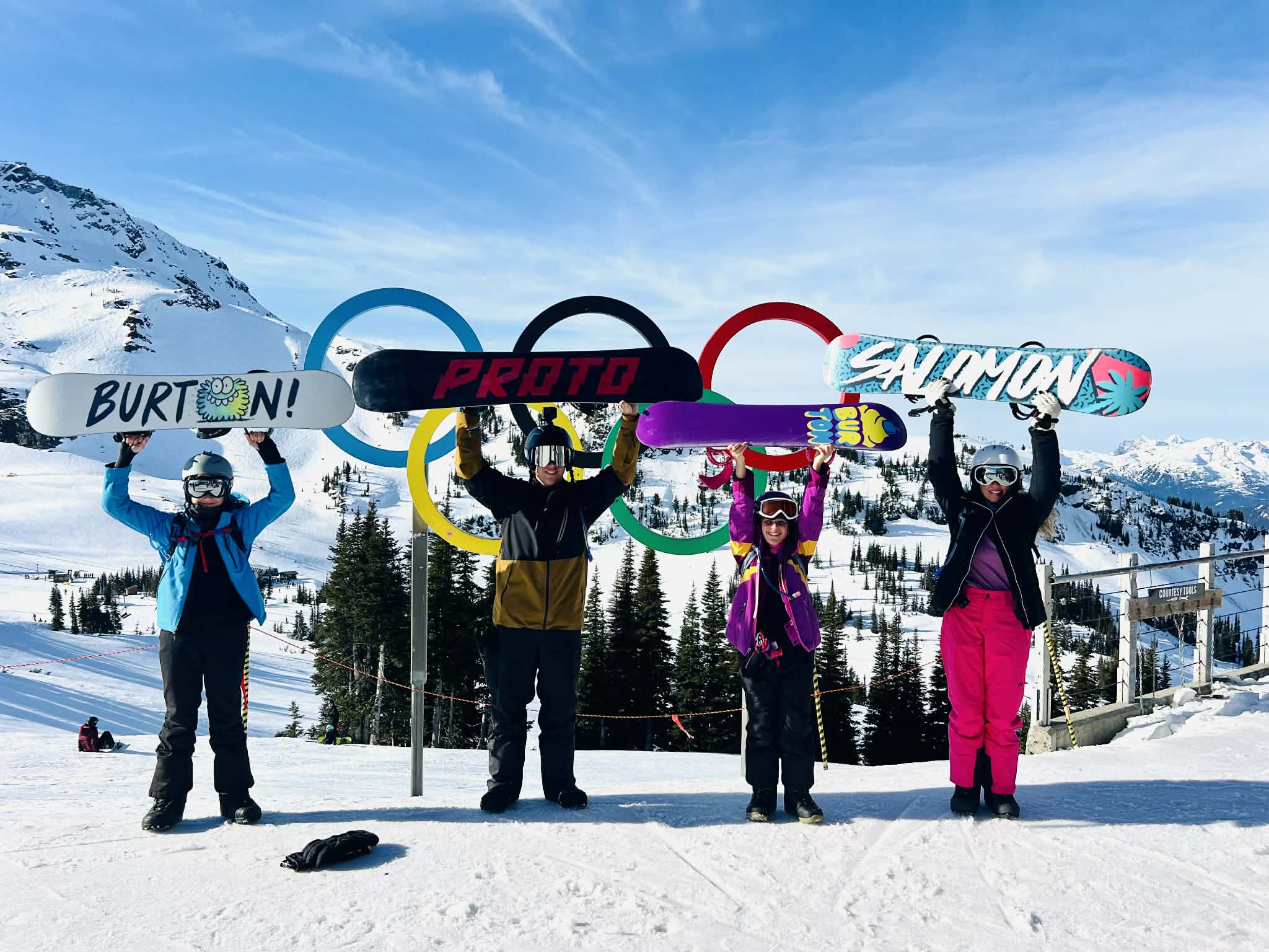 A family holds their snowboards above their heads in front of the Olympic rings at the Whistler Blackcomb mountains.
