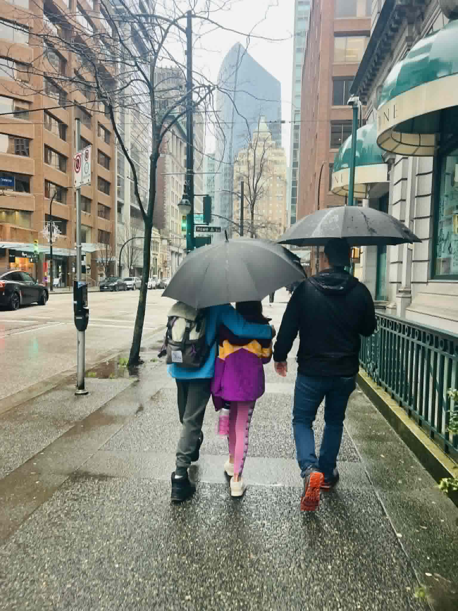 A dad and two kids walking in Vancouver with umbrellas.