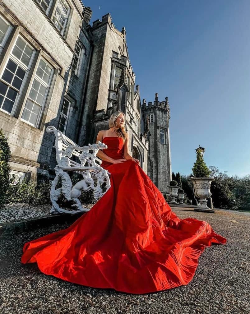 A girl in a red dress sitting in front of the Kinnitty Castle in Ireland.
