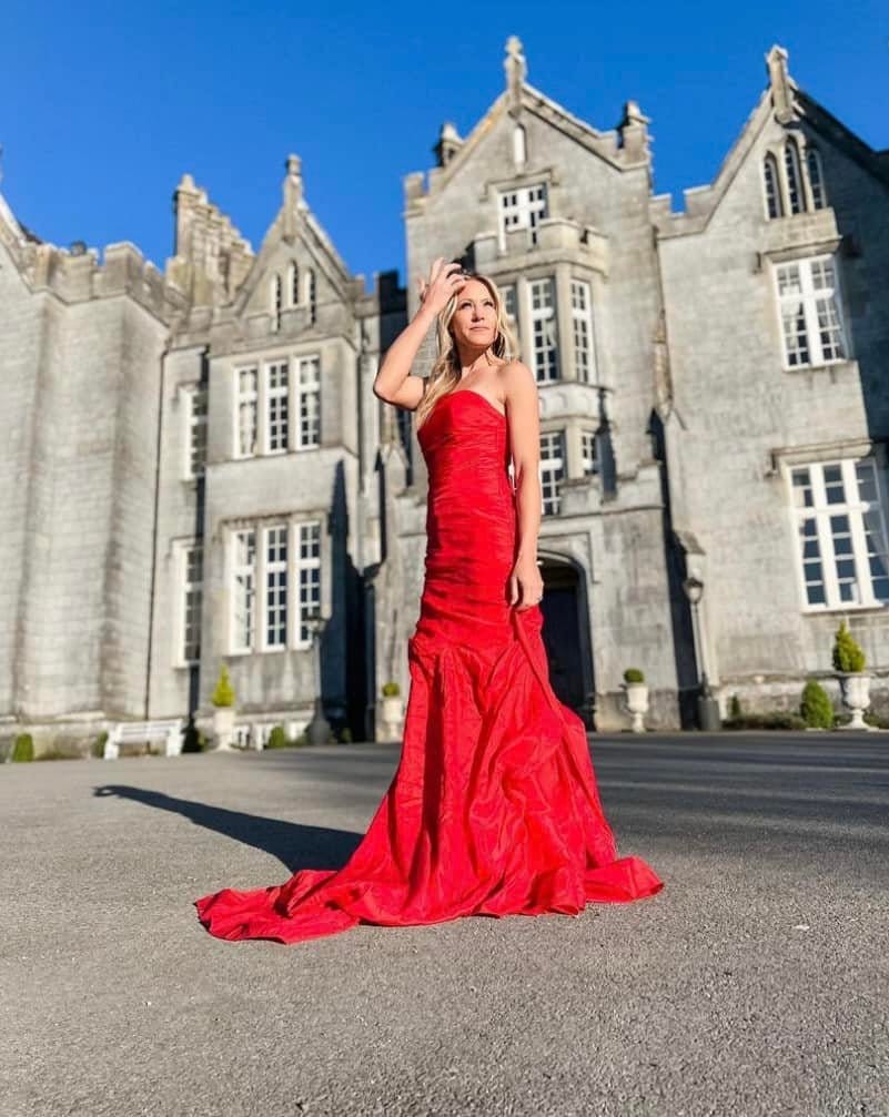 A girl in a red dress standing in front of the Kinnitty Castle in Ireland.