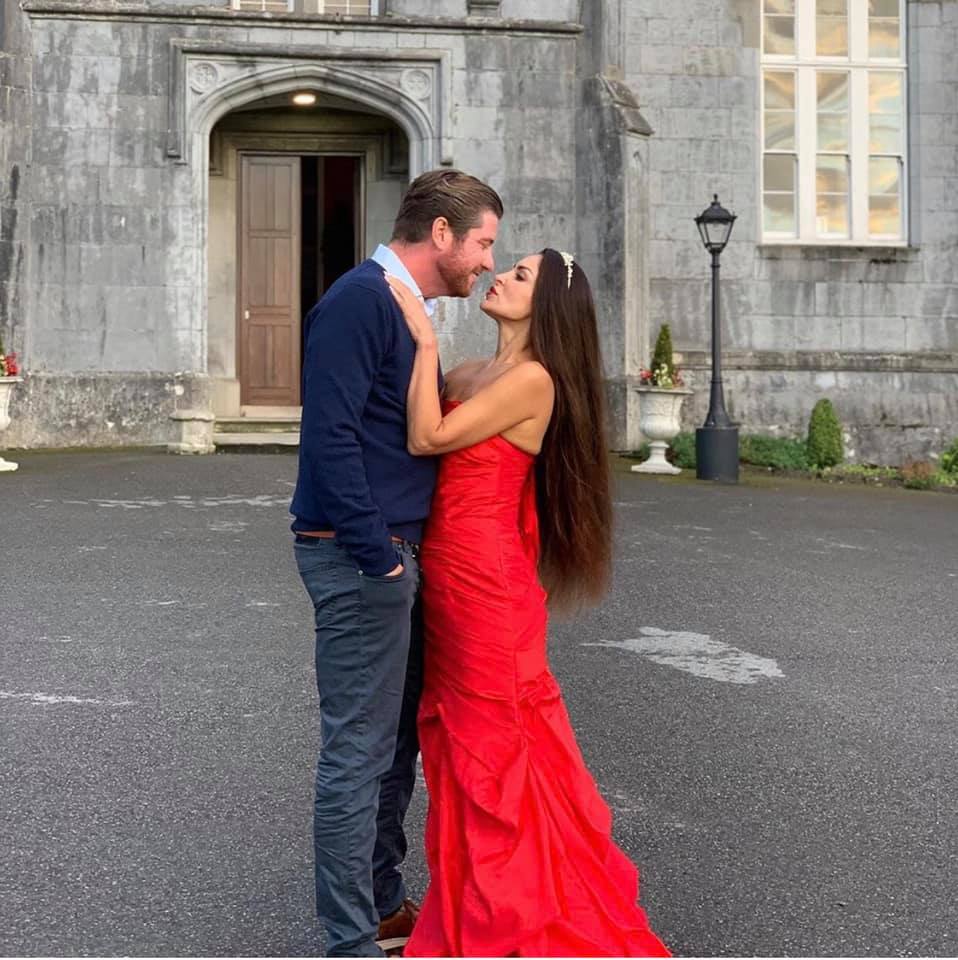 A man and a woman about to kiss. The woman is wearing the Sisterhood of the Castle Dresses red dress.